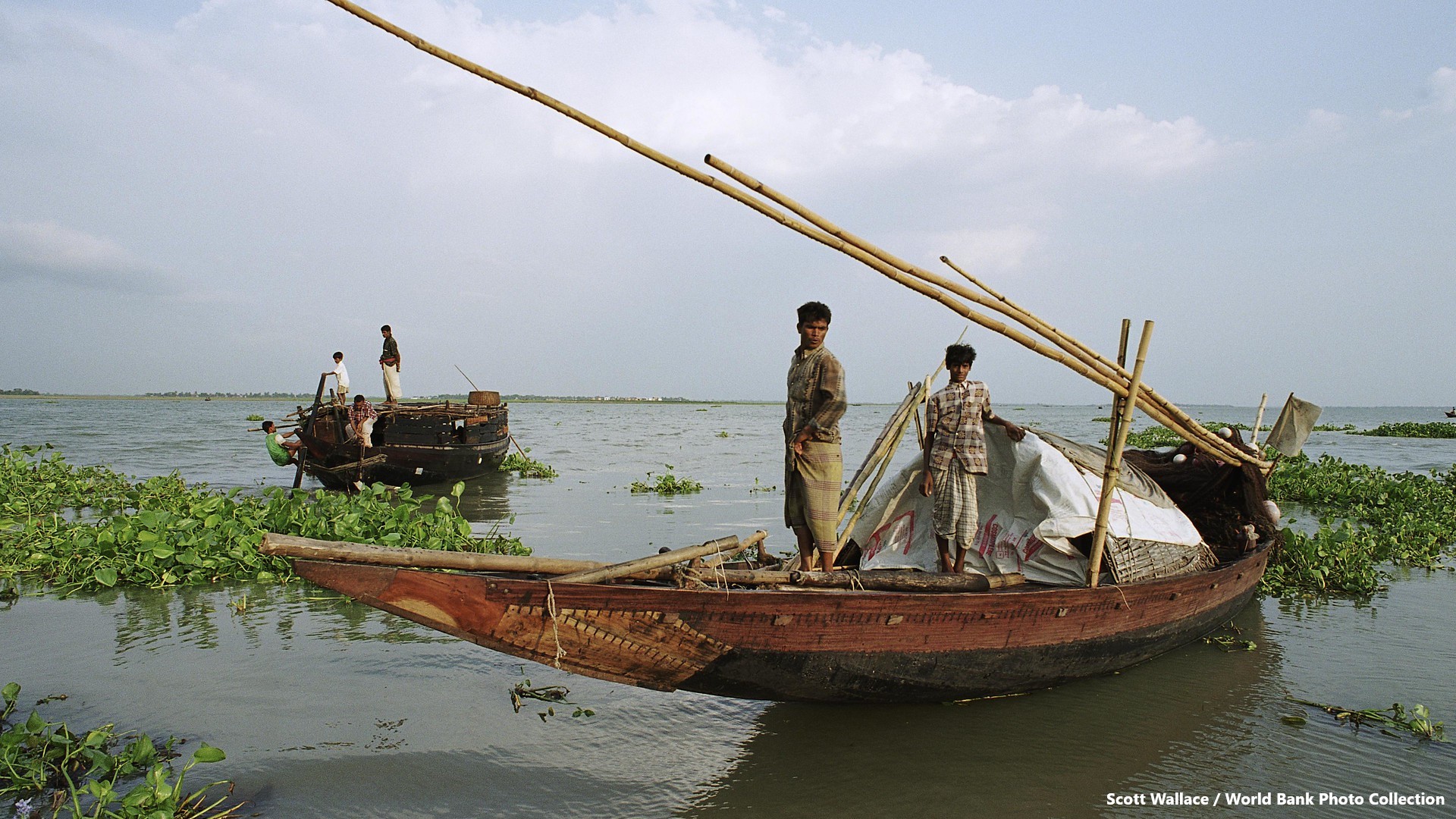 Local boats with cargoes used for transporting goods along rivers and waterways, men and boys punting the boats in shallow water.
