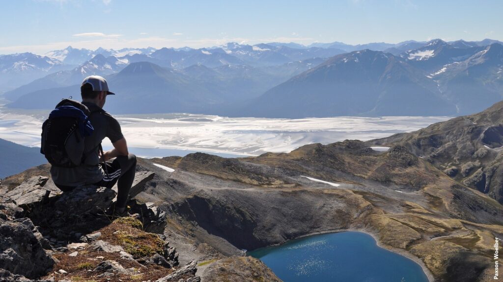 A hiker on the summit of Gentoo Peak, in Alaska's Chugach State Park, with upper Turnagain Arm in the background. Gentoo Peak is one in a handful of prominent peaks and points on the Penguin Ridge traverse between Girdwood and Bird.