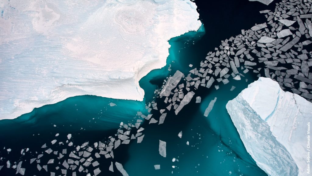 Overhead view of thin sea ice floe fragments between icebergs, failing to form into stable sea ice cover, packed ice and clear blue water.