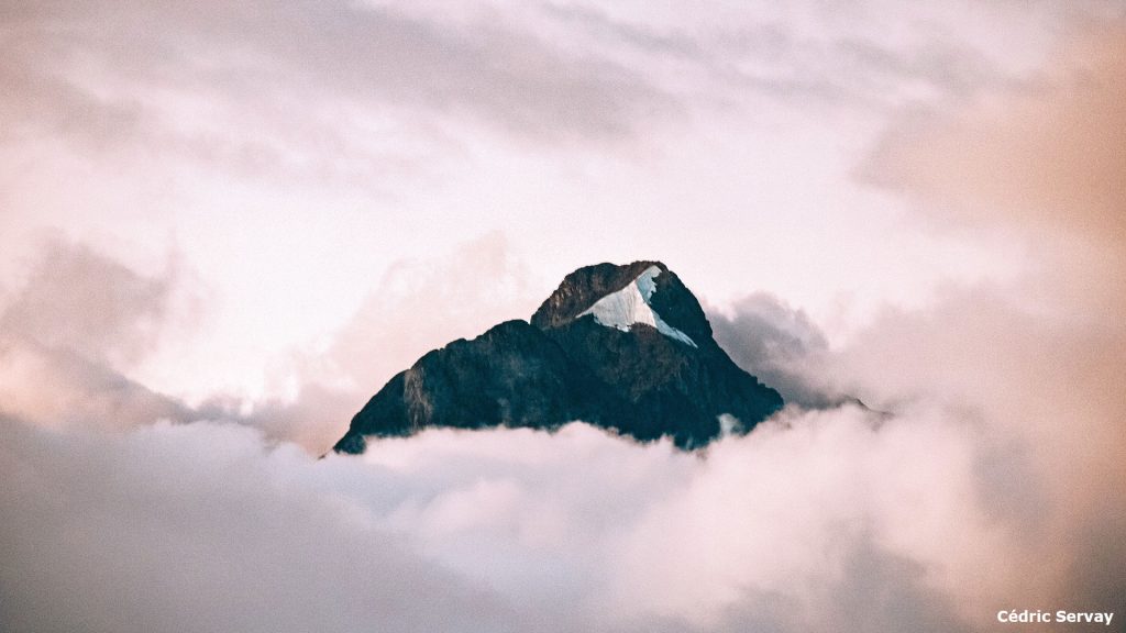 A granite mountain peak rising up above pink-hued clouds