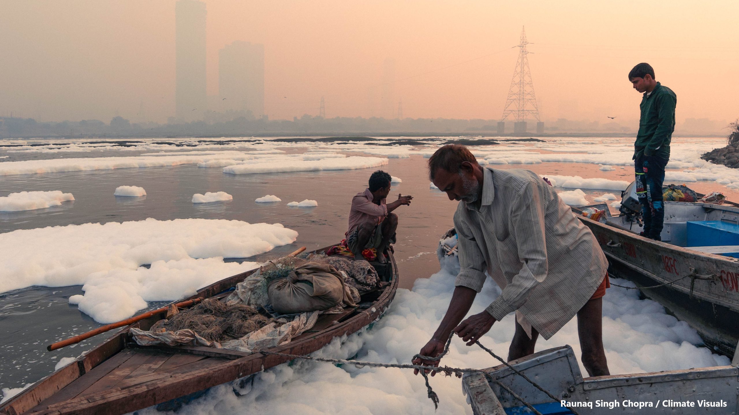 Fishermen on the banks of the river Yamuna, landing the fishing catch, clouds of toxic foam on the water surface, caused by the discharged pollutants from factories.
