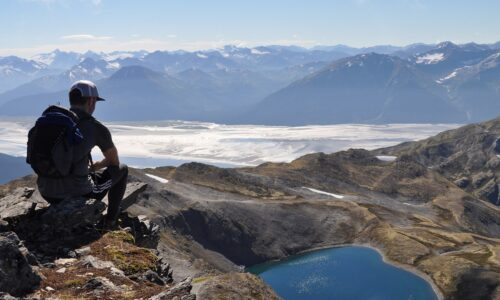 A hiker on the summit of Gentoo Peak, in Alaska's Chugach State Park, with upper Turnagain Arm in the background. Gentoo Peak is one in a handful of prominent peaks and points on the Penguin Ridge traverse between Girdwood and Bird.