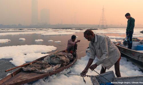 Fishermen on the banks of the river Yamuna, landing the fishing catch, clouds of toxic foam on the water surface, caused by the discharged pollutants from factories.