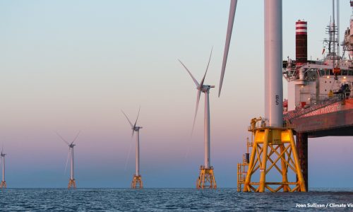 Dusk settles on the Block Island Wind Farm on the last day of construction - 18 August 2016 - of North America's first commercial offshore wind farm, developed by Deepwater Wind, now owned and operated by Ørsted. In this photo, the third blade has just been installed on the fifth and final GE-Alstom Haliade 150-6MW turbine by the Fred Olsen Windcarrier "Brave Tern" (partially seen on the right), which is in the process of jacking down to return to shore. The Block Island Wind Farm is located 3.3 nautical miles SE of Block Island, Rhode Island.